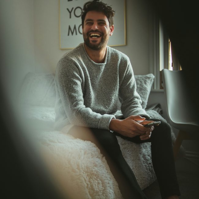 Man sitting on bed laughing Man sitting on bed laughing